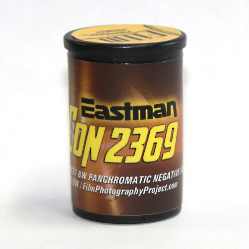 A 35 mm canister in brown and yellow lettered Eastman HI-CON 2369, marked HIGH CONTRAST BW PANCHROMATIC NEGATIVE FILM and FilmPhotographyProject.com