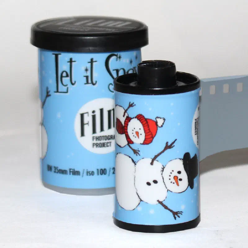 Two pale blue 35 mm cassettes of Let It Snow, snowmen and falling snow around the label, marked BW 35mm Film / iso 100