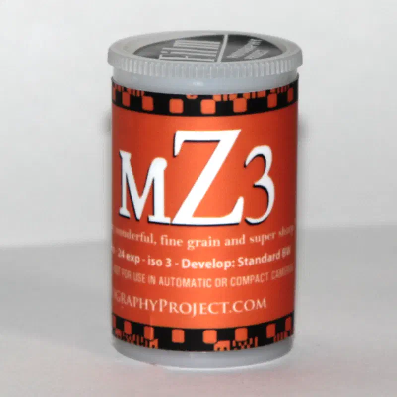 A 35 mm cassette of mZ3, a red label edged top and bottom with sprocket holes, marked 24 exp, iso 3, Develop: Standard BW
