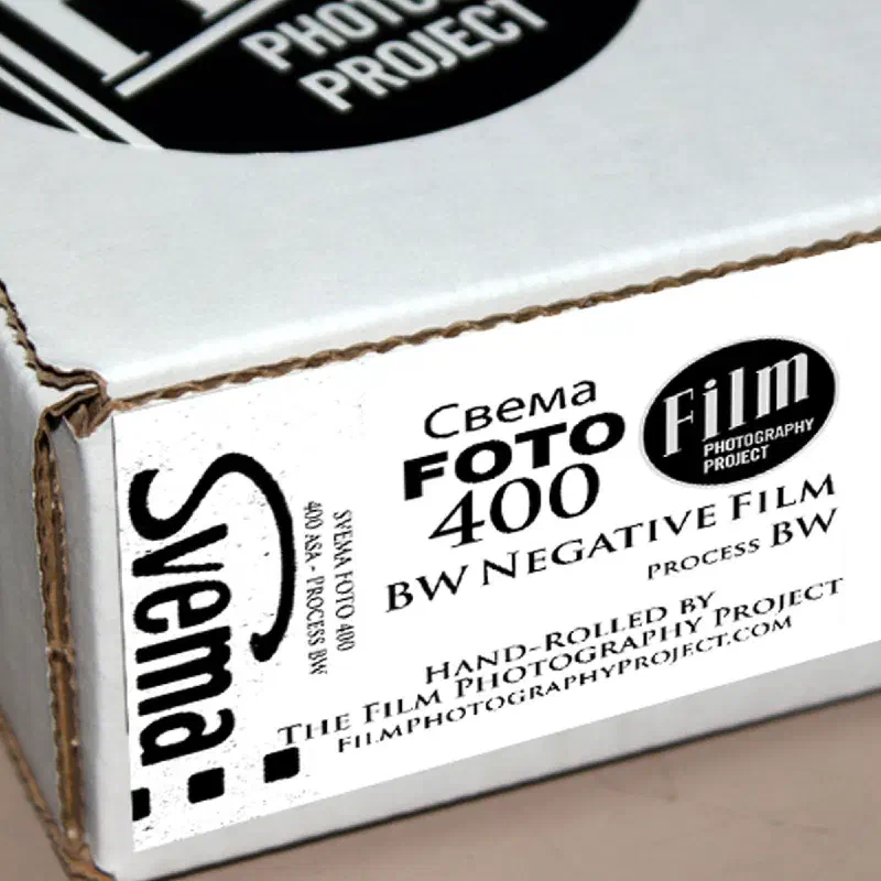 A white Film Photography Project box seen from a front corner, its label reading Свема ФОТО 400 BW NEGATIVE FILM, PROCESS BW, hand-rolled by The Film Photography Project