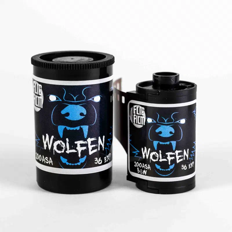 A 35 mm canister and cassette of FLIC FILM Wolfen side by side, a blue snarling wolf on a black label, marked 100ASA B&W 36 EXP