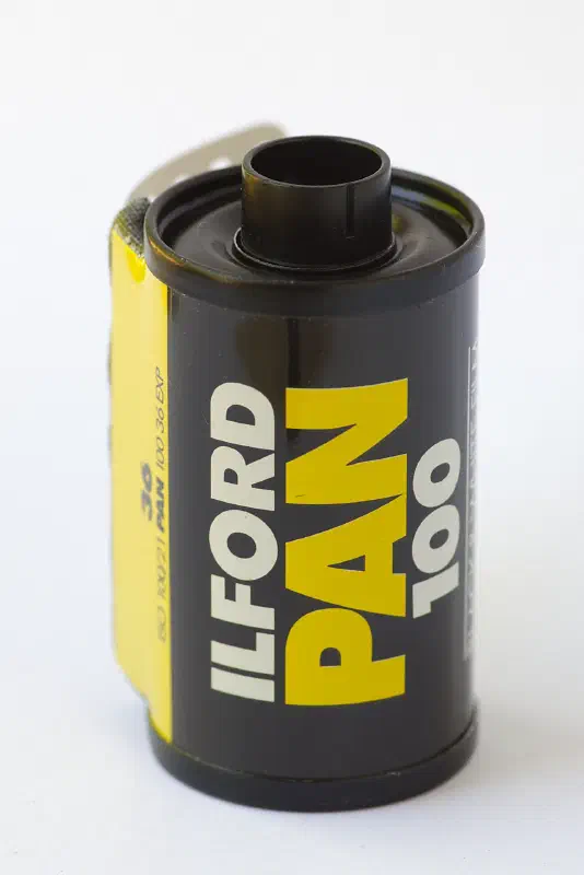 A 35 mm cassette of ILFORD PAN 100, black with a yellow panel lettered in white, marked BLACK AND WHITE FILM