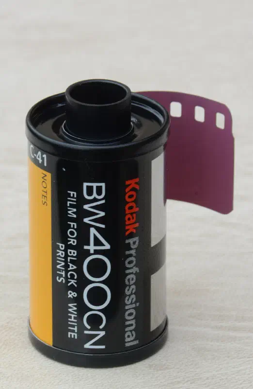 A 35 mm cassette of Kodak Professional BW400CN with its leader out, yellow and white label marked FILM FOR BLACK & WHITE PRINTS and Process C-41