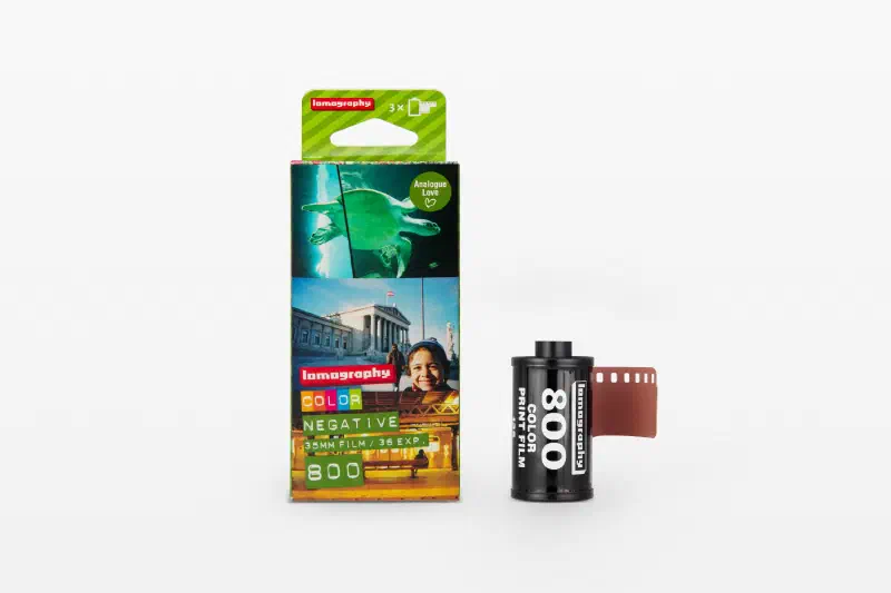 A Lomography Color Negative 800 three-roll carton printed with sample frames, beside a black 35 mm cassette and leader, marked 35MM FILM / 36 EXP