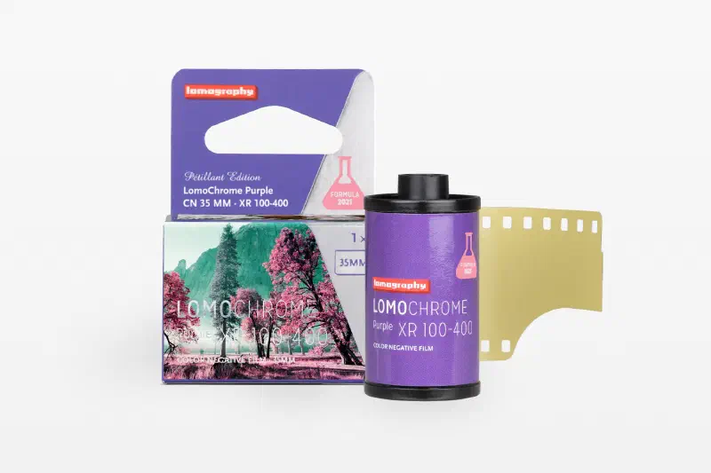 A violet LomoChrome Purple Pétillant carton beside its 35 mm cassette and leader, marked CN 35 MM · XR 100-400 and FORMULA 2021