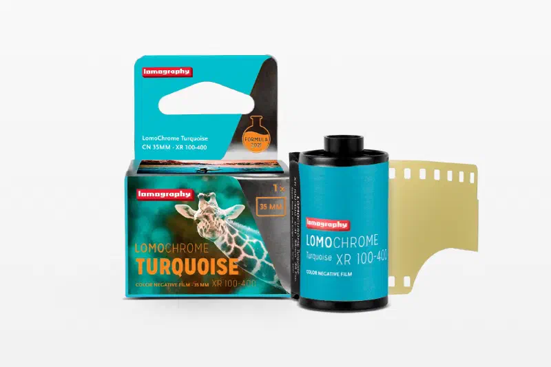 A turquoise LomoChrome Turquoise carton with a giraffe on the front, beside its 35 mm cassette and leader, marked CN 35MM · XR 100-400