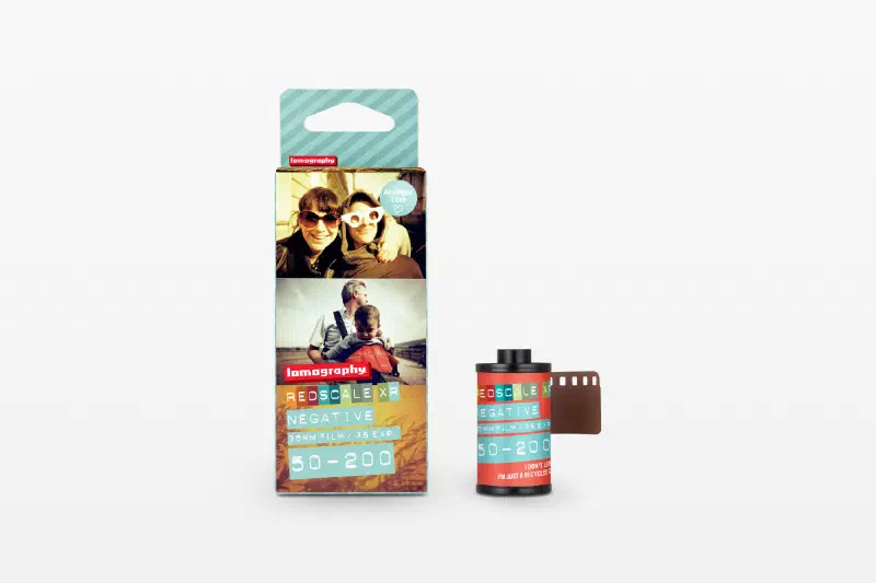A Redscale XR carton printed with sample frames, beside its 35 mm cassette and brown leader, marked 35MM FILM / 36 EXP and 50-200