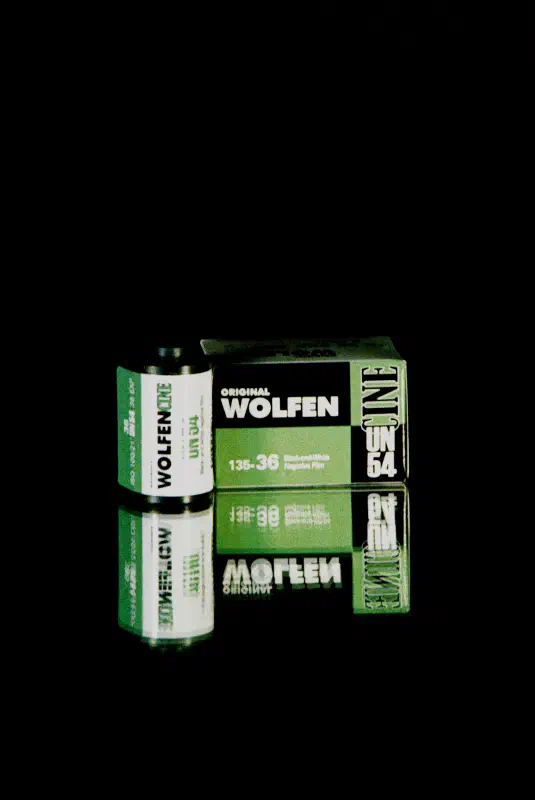 A WOLFEN UN54 carton standing on black beside its 35 mm cassette, both white with a green band