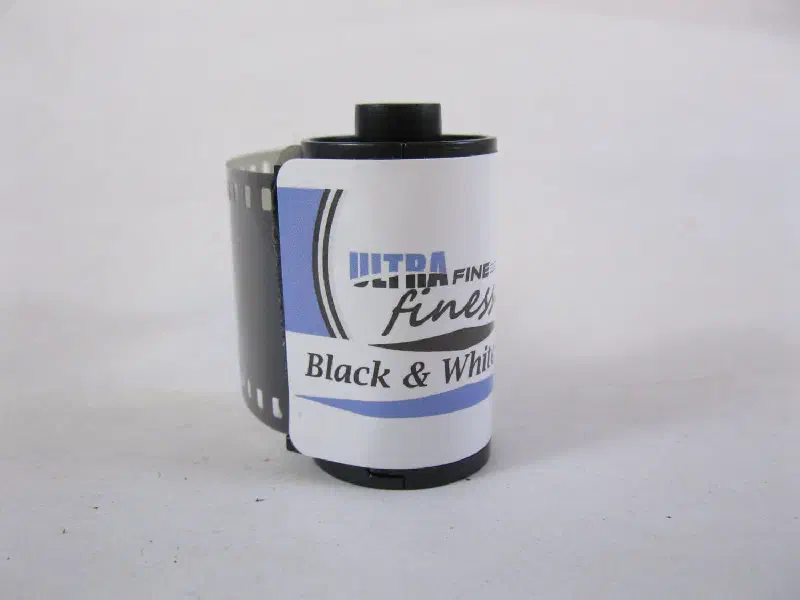 A 35 mm cassette of ULTRA FINE finesse Black & White Film, white label with a blue swash, standing on a plain ground