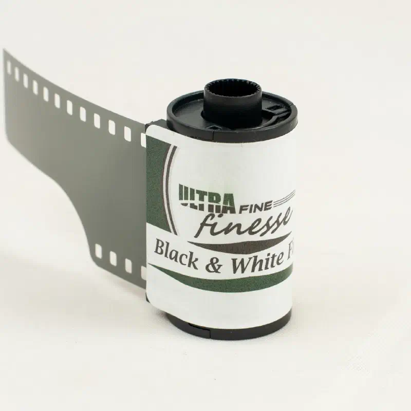 A 35 mm cassette of ULTRA FINE finesse Black & White Film with its leader pulled out, white label with a green swash